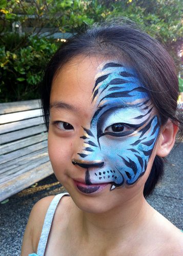 A girl in a blue half face tiger face-paint